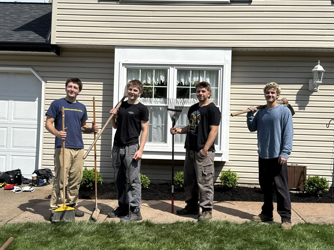 Four crew members with yard tools in front of a house