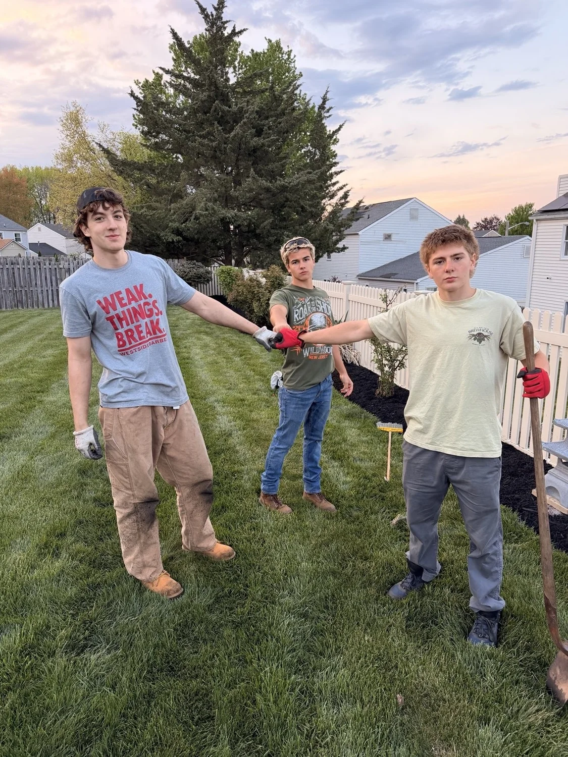 Three crew members with work gloves and tools in a backyard