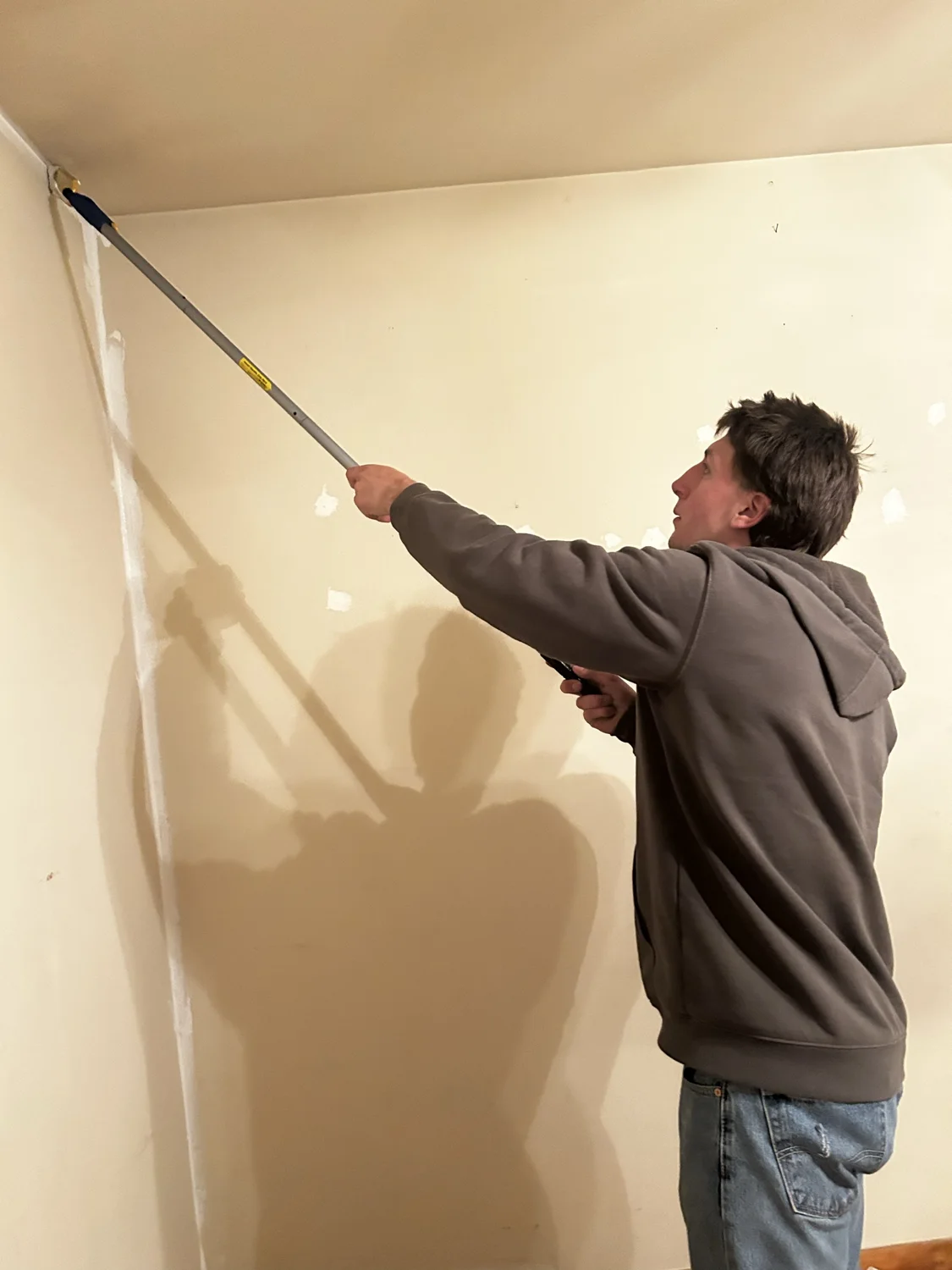 A crew member painting an indoor wall with a roller