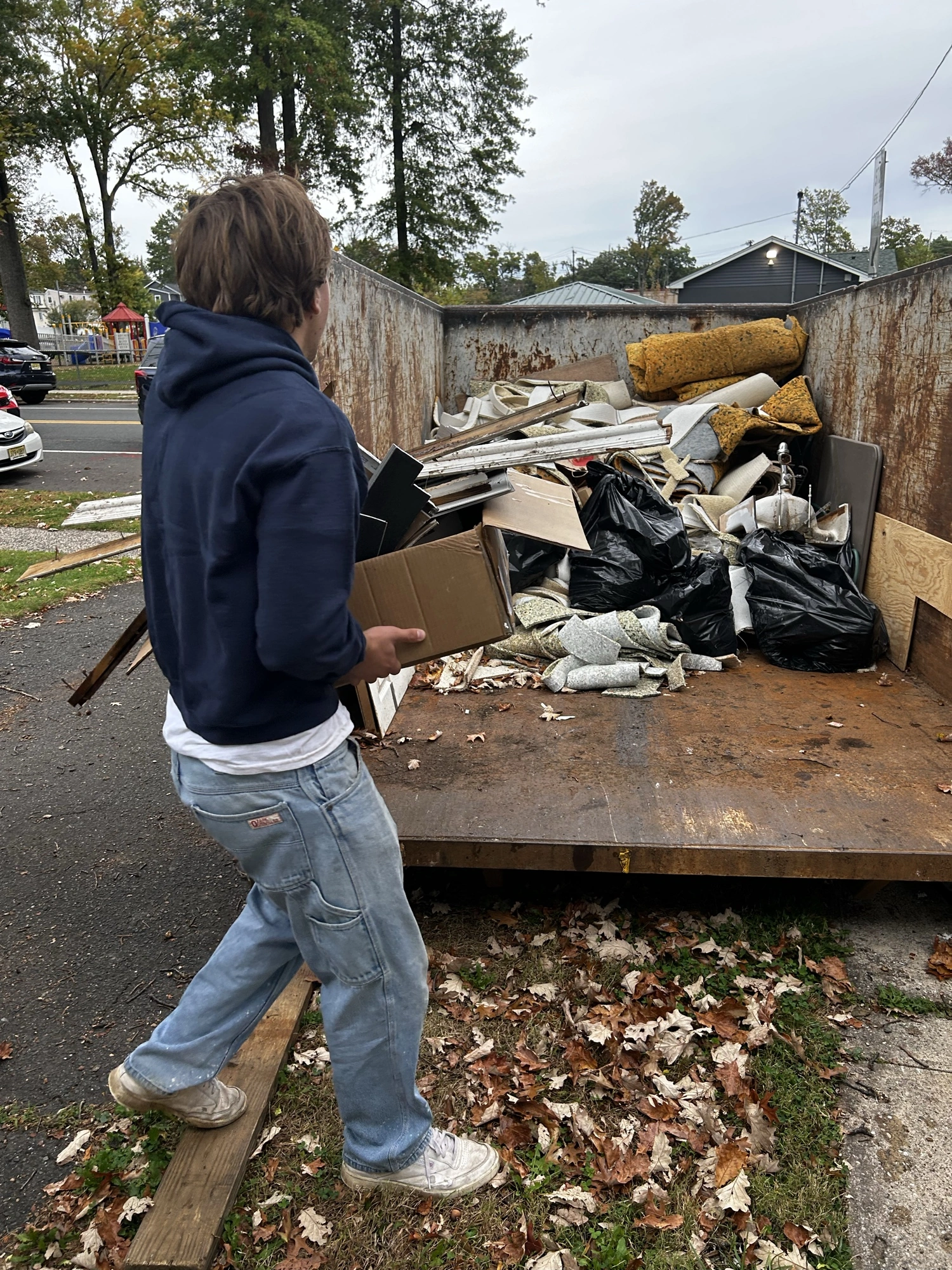 A crew member carrying debris to a dumpster during a cleanup